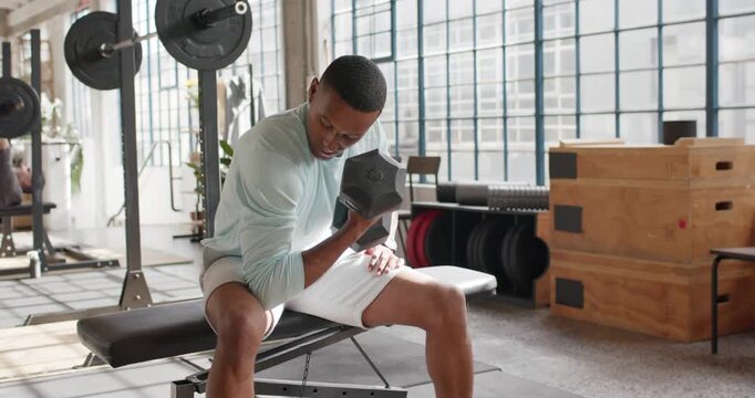 Adult African American man in mint top leaning reaching hex dumbbell curling on bench toning arms