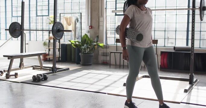 Woman wearing leggings carrying roller to mat in gym placing it, sitting doing leg lifts recovering