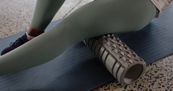 African American 30s woman targeting ache placing foam roller under right thigh on blue mat rolling