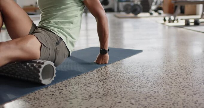African American adult male entering gym on blue-mat placing foam-roller under right thigh for ease