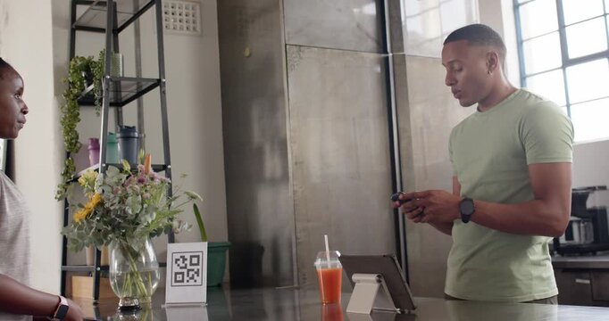 African American man and woman speaking at cafe, checking tablet while tapping reader and paying