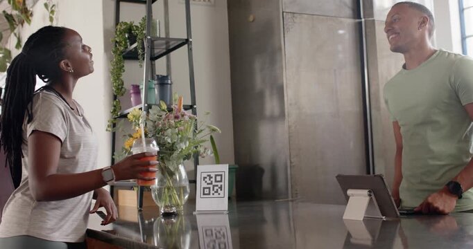 African woman in 20s collecting order at cafe, staff handing cup, patrons talking, copy space