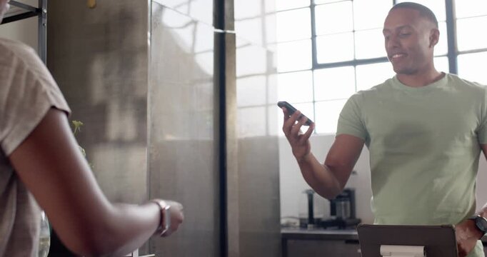 Male cashier taking phone at cafe after client holding watch using tablet closing sale, copy space