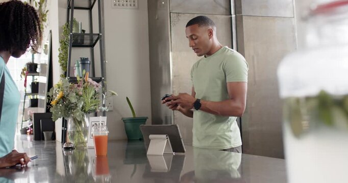 African American server offering reader at cafe counter, customer coming and tapping phone to pay
