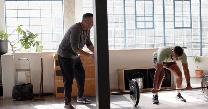 Diverse training pair walking left cueing trainee gripping barbell and deadlifting in sunlit loft
