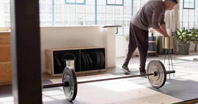 Man retrieving chalk, stepping to loaded barbell in loft studio wearing workout gear preparing lift