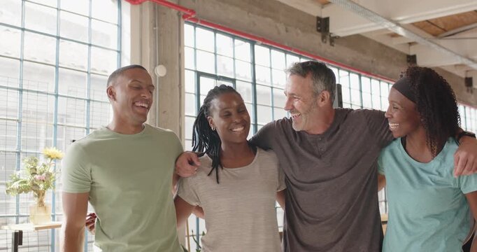 Diverse friends in activewear linking arms after workout, leaning and laughing in studio by windows