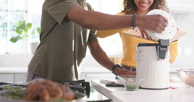 Couple preparing meal at kitchen island, woman tipping cutting board, man lifting compost lid