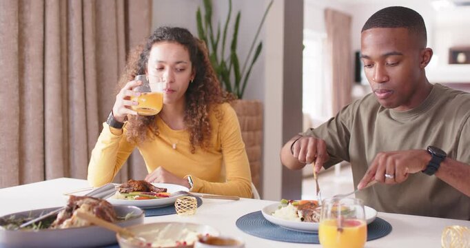 Couple at home starting meal, African American man cutting, woman sipping juice with utensils