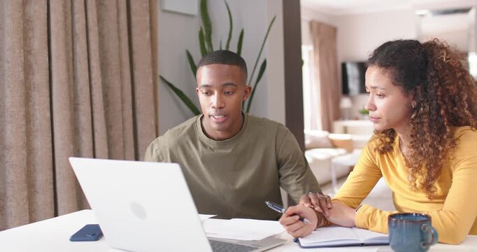 Couple sitting at white table at home, man holding paper, pointing at laptop, woman taking notes