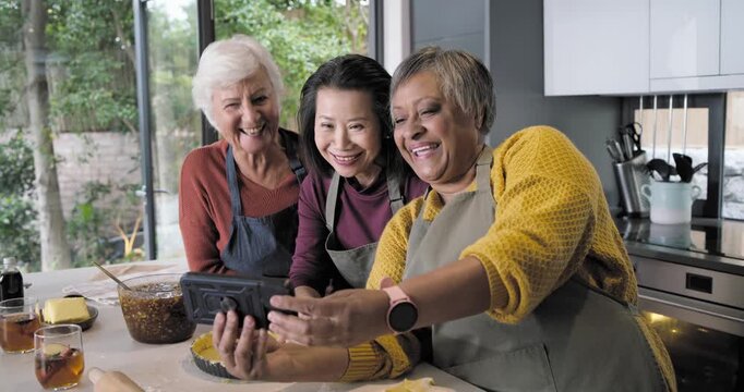 Diverse female cooks pressing pastry into tart in kitchen pulling smartphone taking selfies for fun
