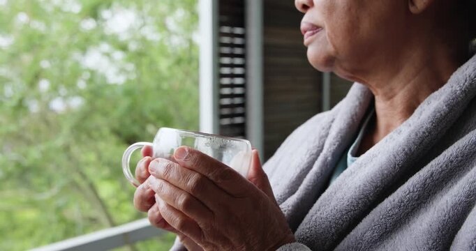 Senior African American lady on balcony in robe cupping mug with pink patches, sipping, copy space
