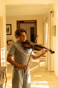 pre teen boy playing violin indoors at sunset