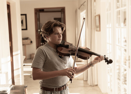 pre teen boy playing violin indoors at sunset