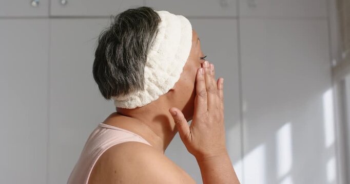African woman pressing cheek by ear, massaging jaw at vanity with headband for skincare, copy space