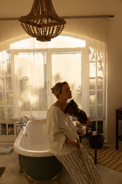 portrait of young woman playing violin in bathroom at sunset
