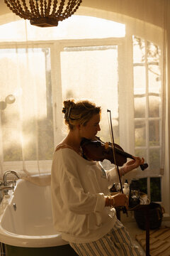 portrait of young woman playing violin in bathroom at sunset