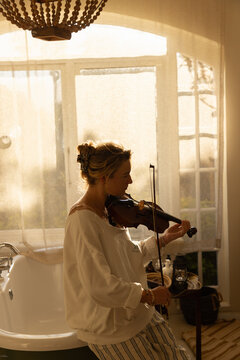 portrait of young woman playing violin in bathroom at sunset