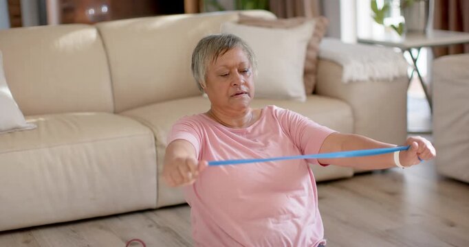 Senior African American woman sitting in living room holding band taut, pulling inward for strength