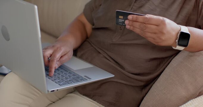 Adult is entering payment details on laptop after checking card chip while seated on beige couch