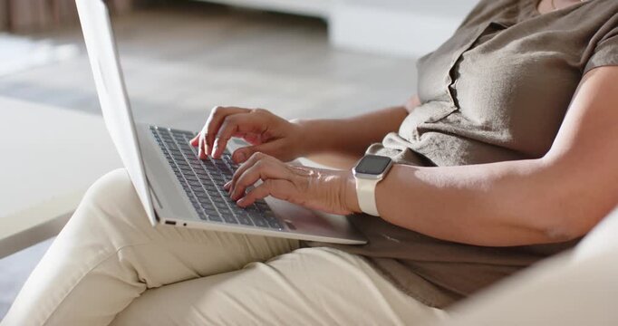 African American woman starting with hands poised, typing on silver laptop on sofa, finishing work
