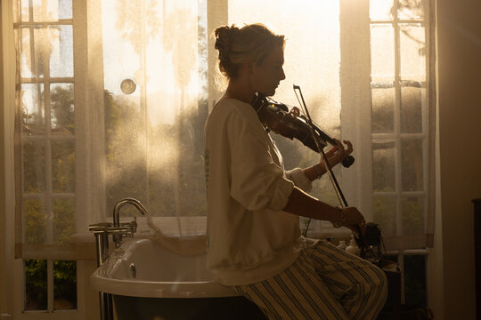 portrait of young woman playing violin in bathroom at sunset