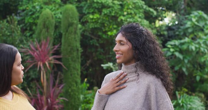 Two African women talking in garden, turtleneck speaker raising hand-to-chest, sharing feelings