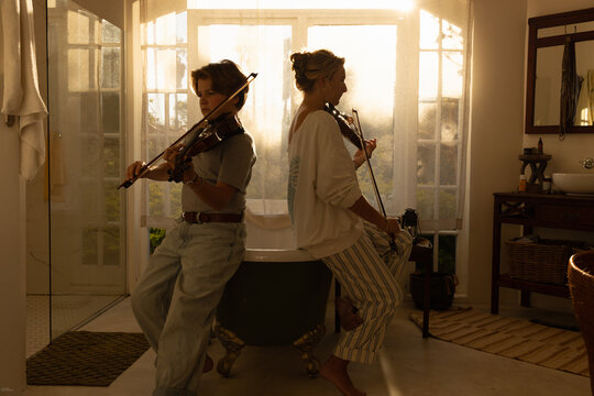 young woman and pre teen boy playing violin at sunset indoors