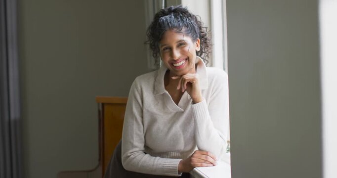 African American woman sitting at window, resting elbow on windowsill, smiling following camera cue