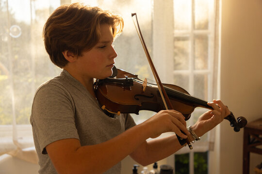 pre teen boy playing violin indoors at sunset