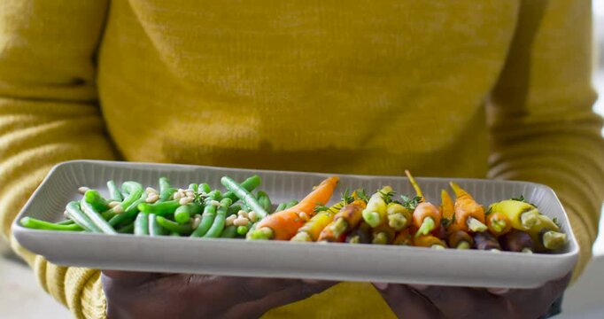 Person in mustard sweater is lowering platter after small hand shift to display veggies near window