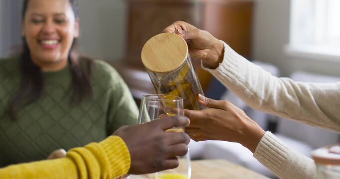 Adult African American woman smiling at table as person pouring carafe after empty glass meal start