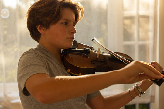 pre teen boy playing violin indoors at sunset
