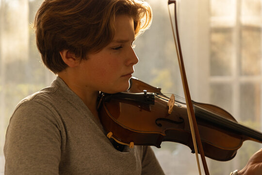 pre teen boy playing violin indoors at sunset