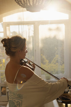 portrait of young woman playing violin in bathroom at sunset