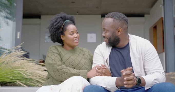 African American couple sitting on steps, holding hands after shared laugh, leaning, showing love