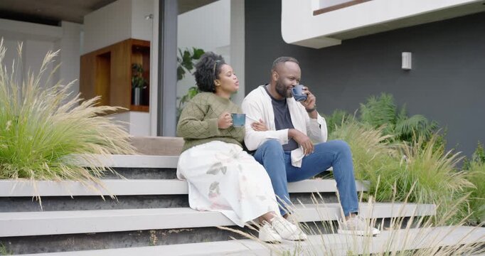 African couple sitting on wide wooden porch steps, sipping blue mugs and sharing affection