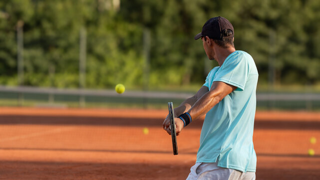 Young professional tennis player performing backhand shot during practice on clay court in warm evening light. Focus on technique, athletic performance, training and healthy active lifestyle.