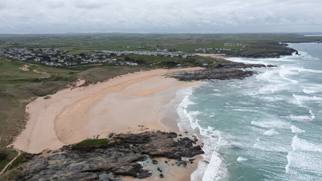 Aerial view of Constantine Bay featuring its wide sandy beach, rugged rocky outcrops, and rolling green hills under an overcast sky in Padstow, Cornwall, United Kingdom.