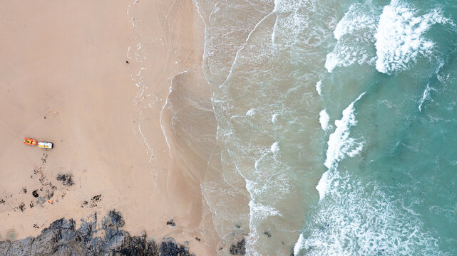 Aerial view of Constantine Bay with turquoise waves crashing on the sandy shore and a small boat on the beach in Padstow, Cornwall, United Kingdom.