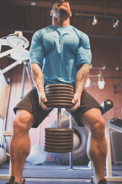 Muscular man straining while lifting heavy weights at gym