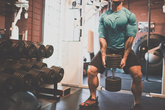 Muscular man with tattoos lifting heavy dumbbell