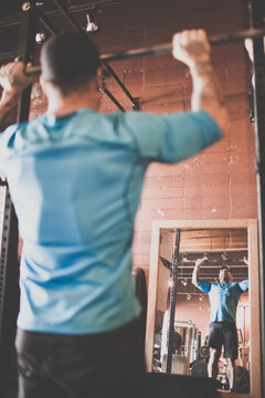 Rear view of man lifting barbell above his head, view in mirror
