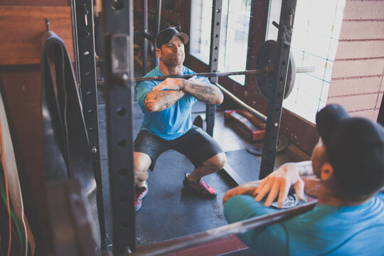 Tattooed man preforming front squats at the gym