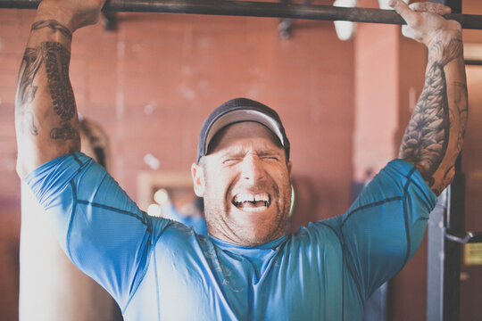 Tattooed man yelling while lifting heavy barbell