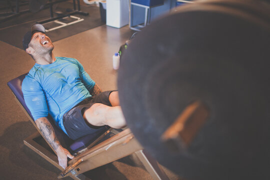 Tattooed man grimacing while lifting heavy weights with his legs