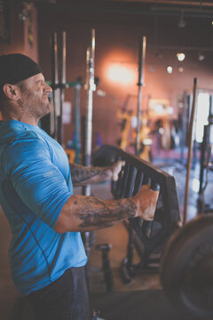 Tattooed man grimacing while lifting heavy weights