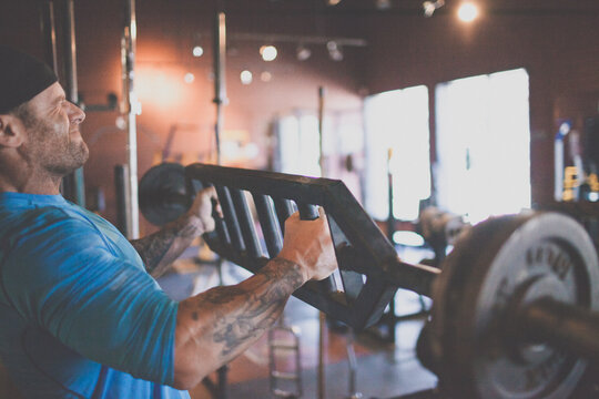Tattooed athlete lifting a heavy barbell at gym