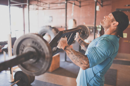 Tattooed athlete lifting a heavy barbell at gym