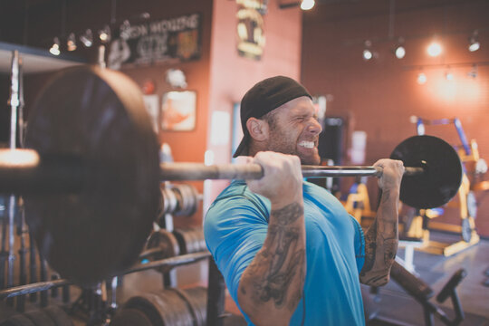 Strong man with tattoos preforms bicep curls using barbell